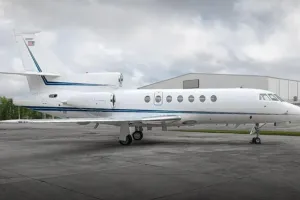 Full side profile of the 2002 Falcon 50EX for sale, showcasing its distinctive three-engine design and blue stripe livery